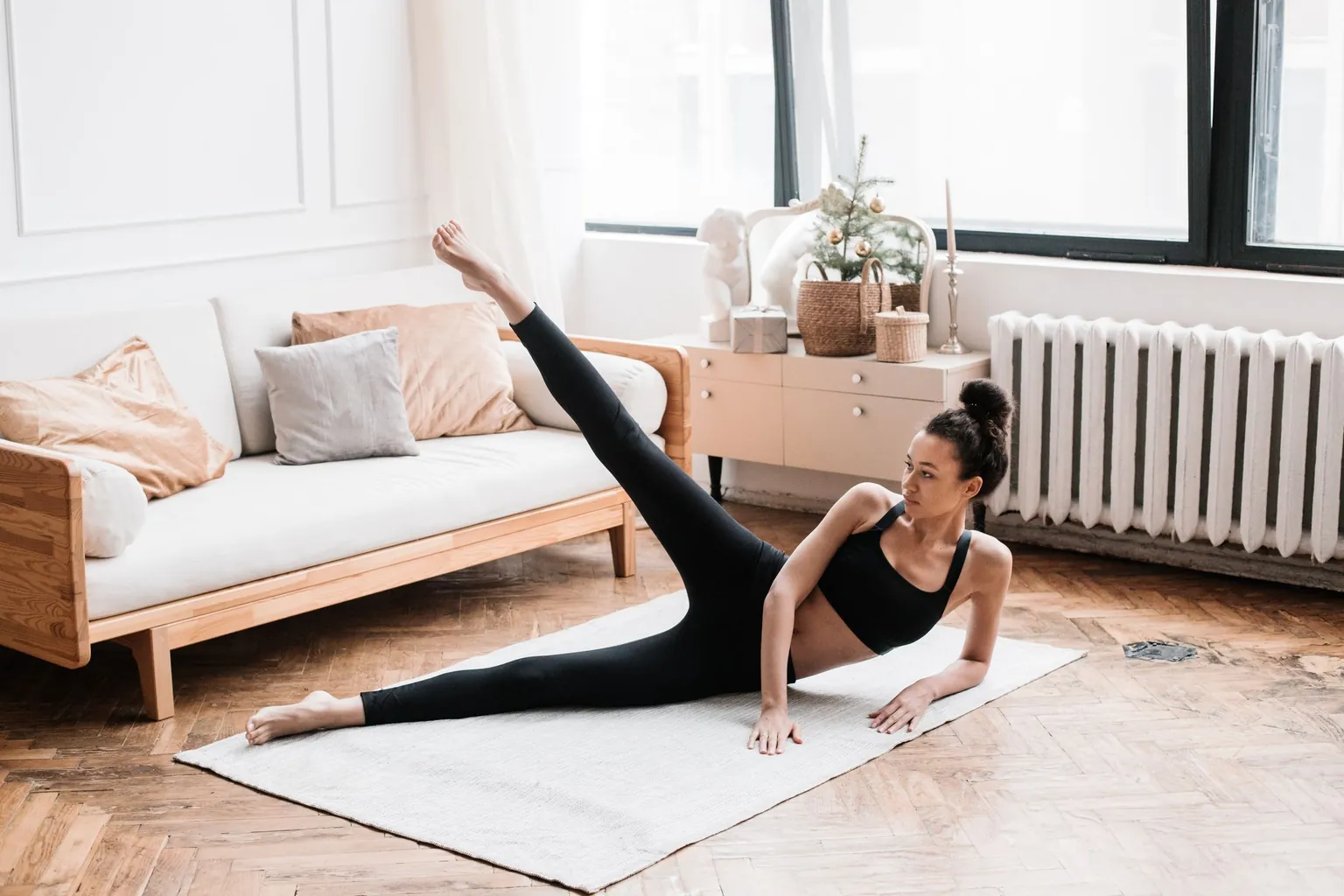 Femme allongée sur le côté sur un tapis qui lève la jambe du dessus, dans un salon
