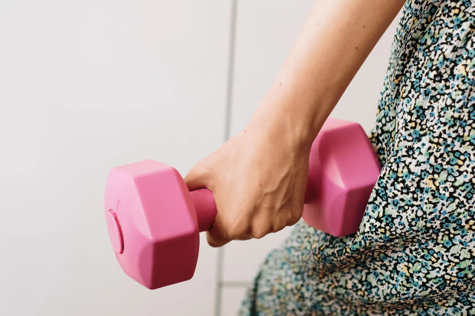 Main de femme tenant un petit haltère rose en plastique, à la maison