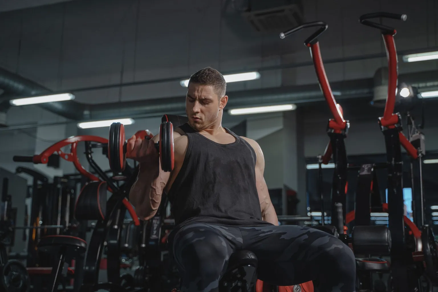 Homme assis dans une salle de musculation réalisant un curl biceps avec un haltère