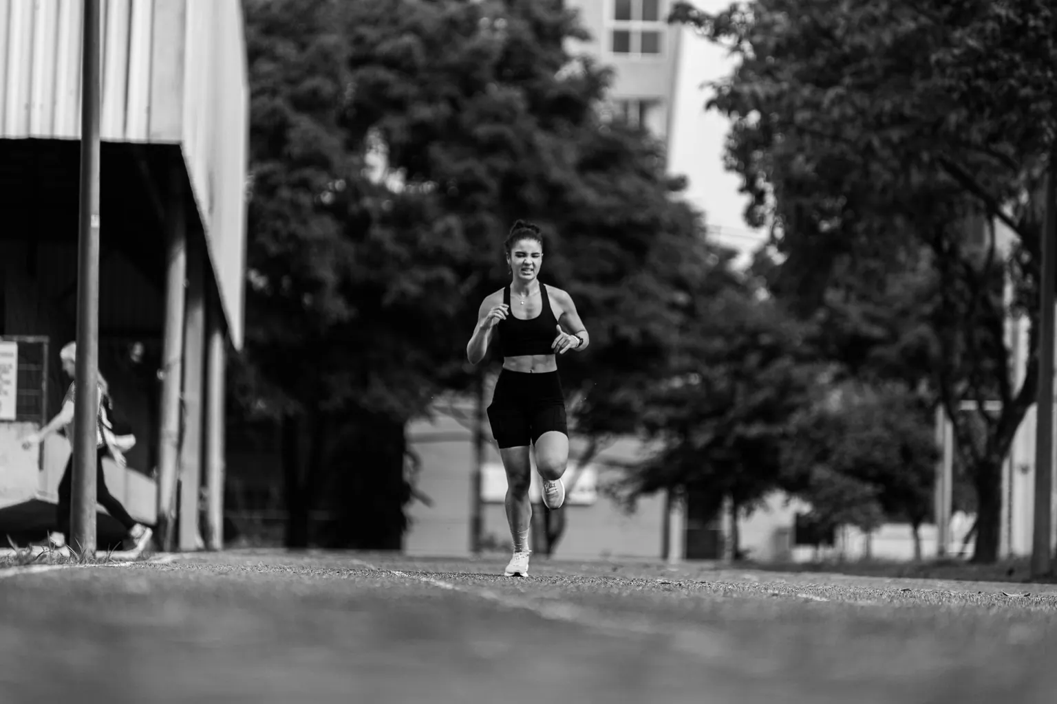 Femme en tenue de sport courant sur une piste extérieure, photo en noir et blanc