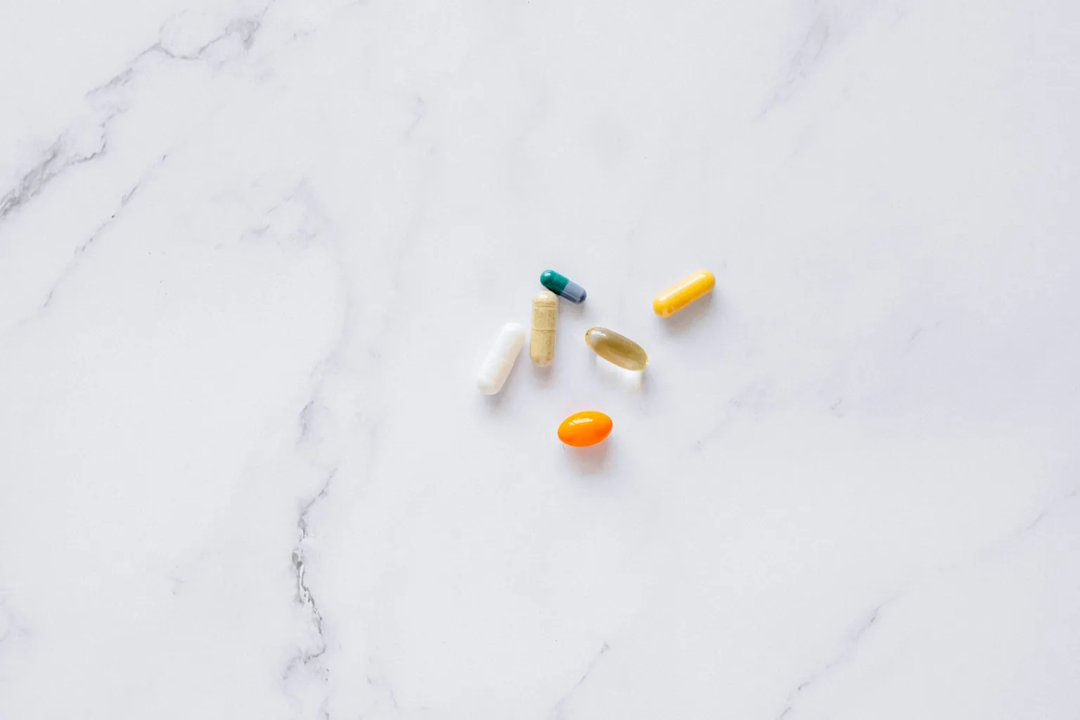 Six gélules et capsules de couleurs différentes posées sur un plan de marbre blanc