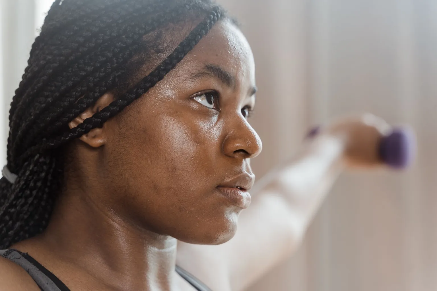Femme vue de profil, bras tendu devant elle avec un petit haltère violet