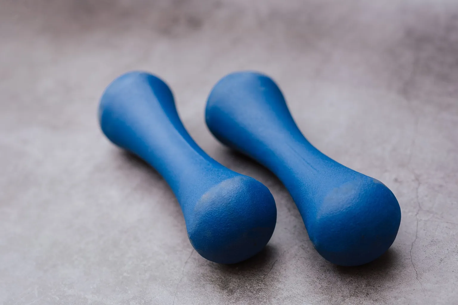 Deux petits haltères bleus en vinyle posés côte à côte sur un sol gris