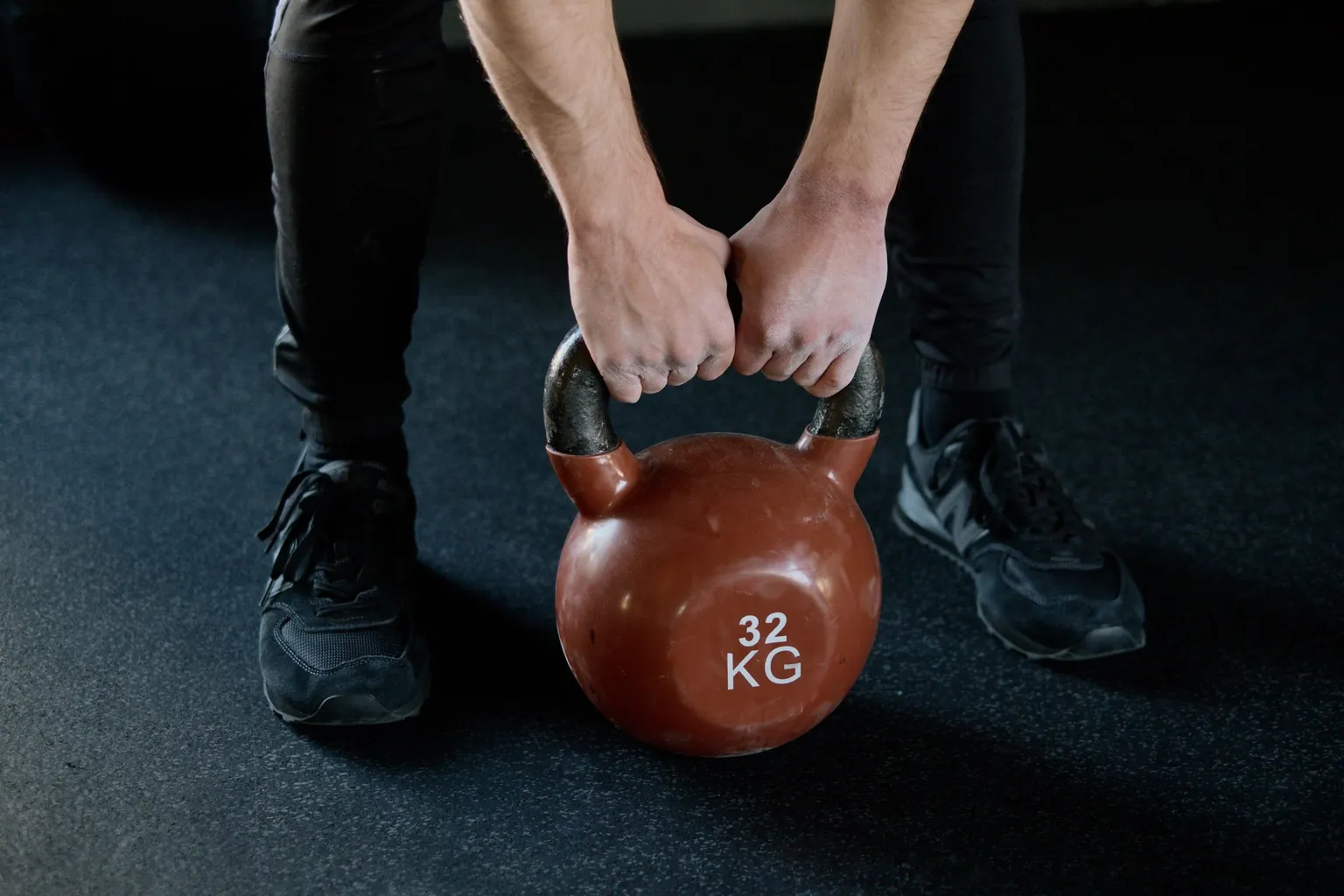 Deux mains serrant ensemble la poignée d’un kettlebell posé au sol