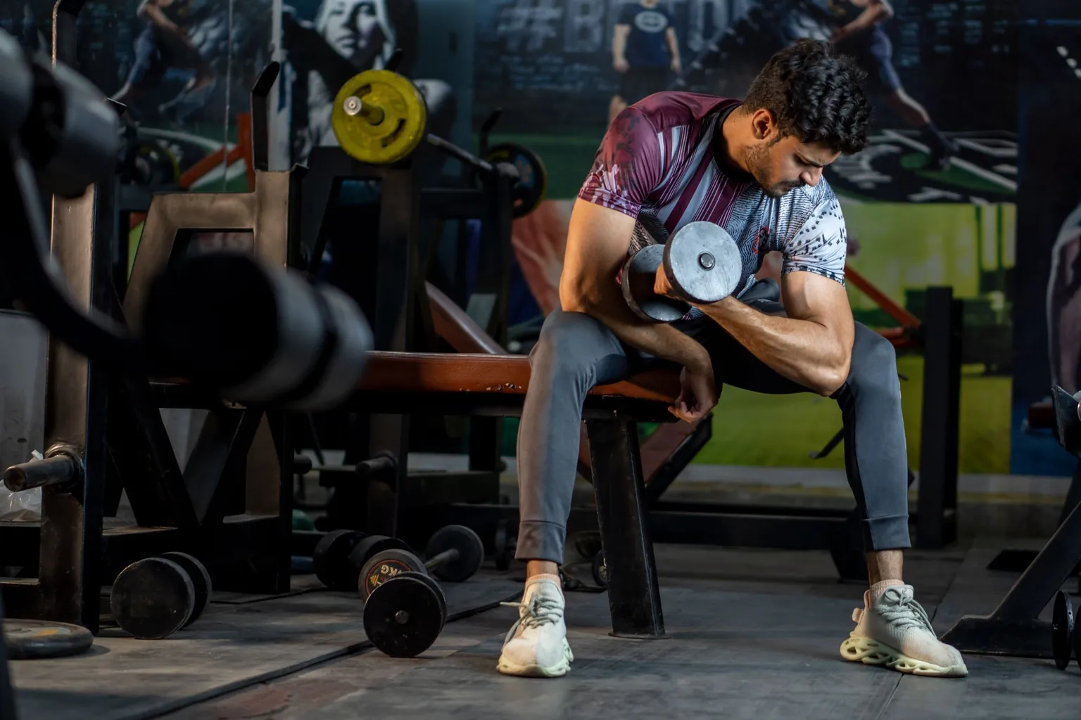 Homme assis sur un banc de musculation réalisant une flexion du coude avec un haltère