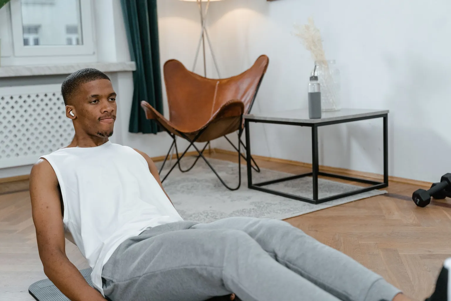 Homme assis sur un tapis dans un salon, buste incliné en arrière et jambes tendues, en exercice abdominal