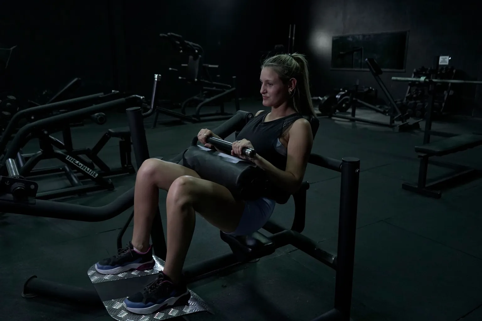 Femme installée sur une machine de hip thrust guidée, coussin posé sur les hanches, pieds à plat sur la plateforme