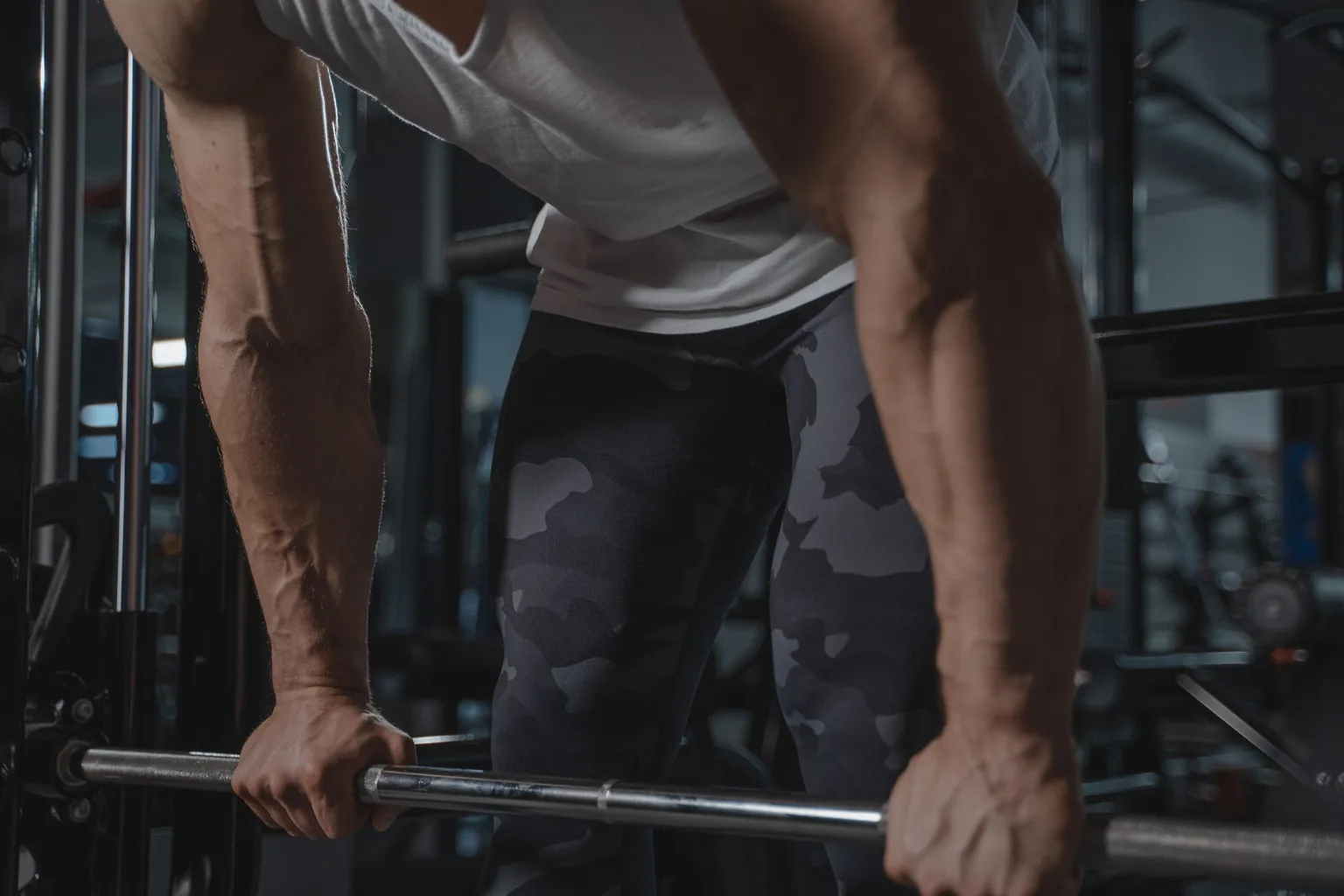 Homme penché en avant saisissant une barre de musculation à deux mains dans une salle de sport