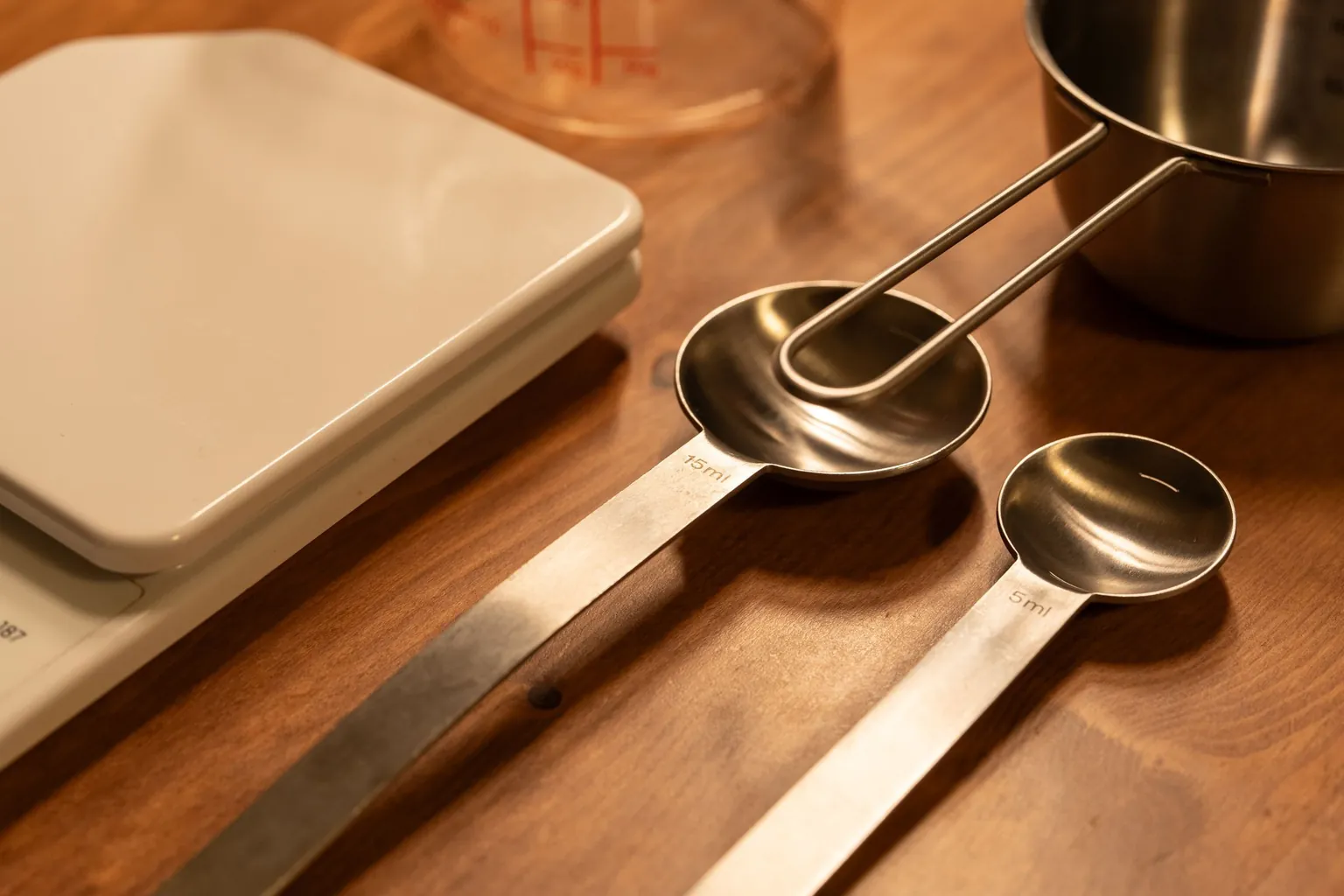 Cuillères doseuses de 5 et 15 ml et balance de cuisine posées sur une table en bois