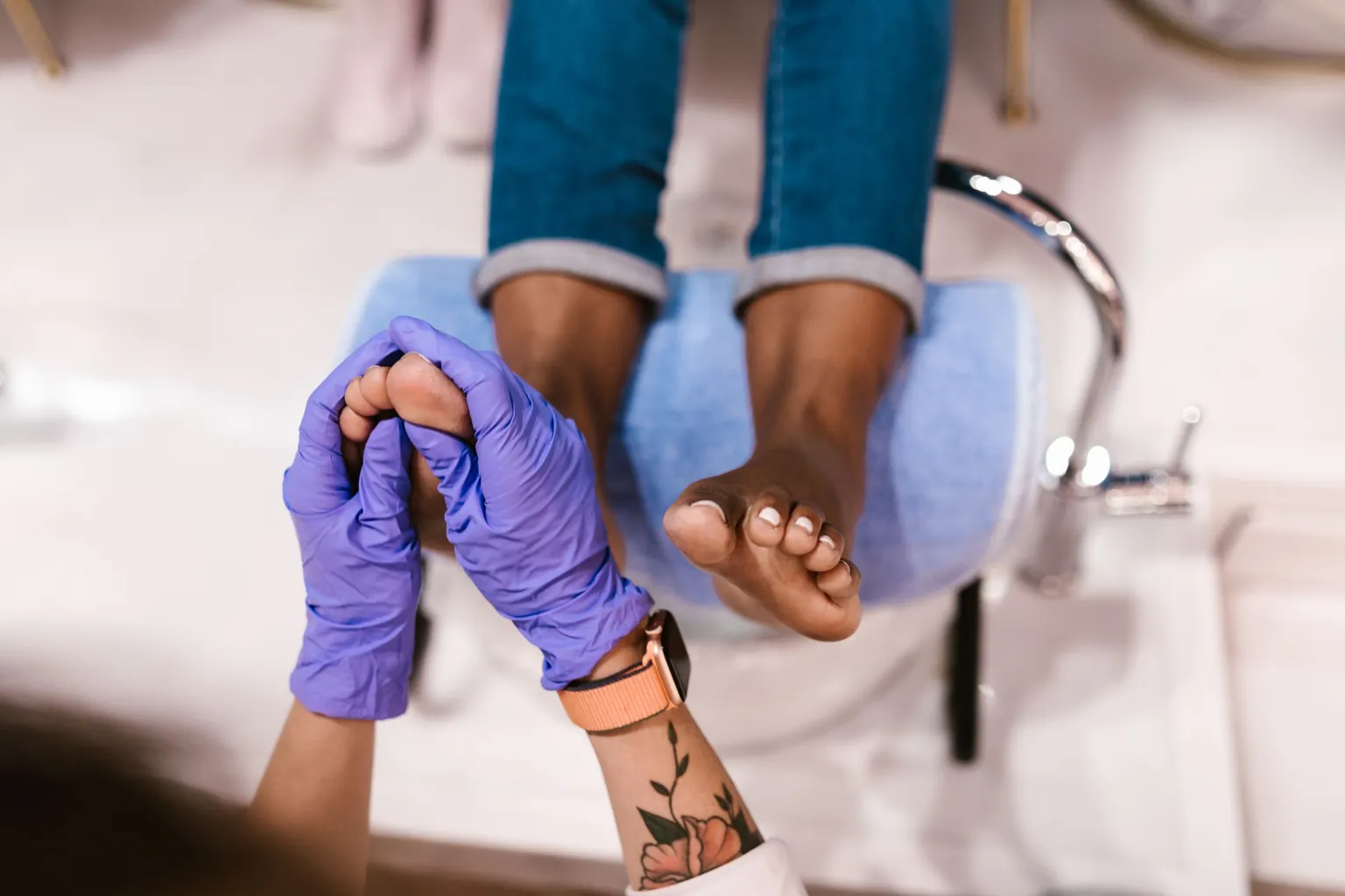 Soin des pieds au-dessus d'un bac de pédicure, mains gantées tenant un pied