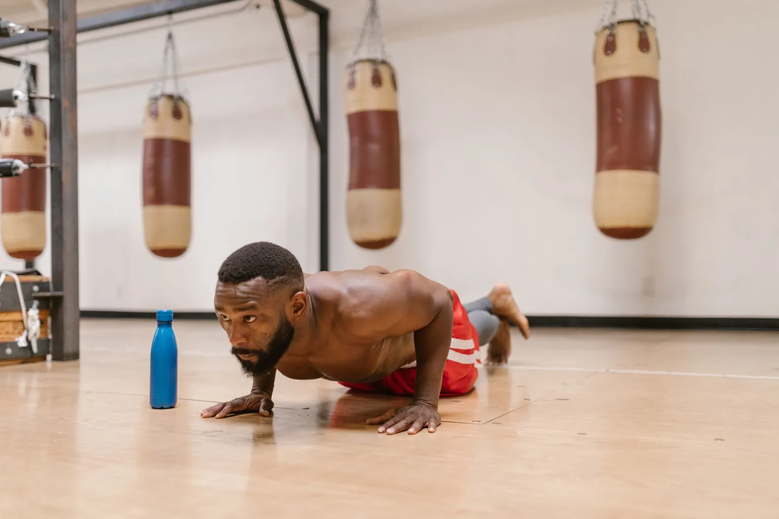 Homme en appui sur les mains au sol d'une salle de boxe, corps tendu des épaules aux pieds