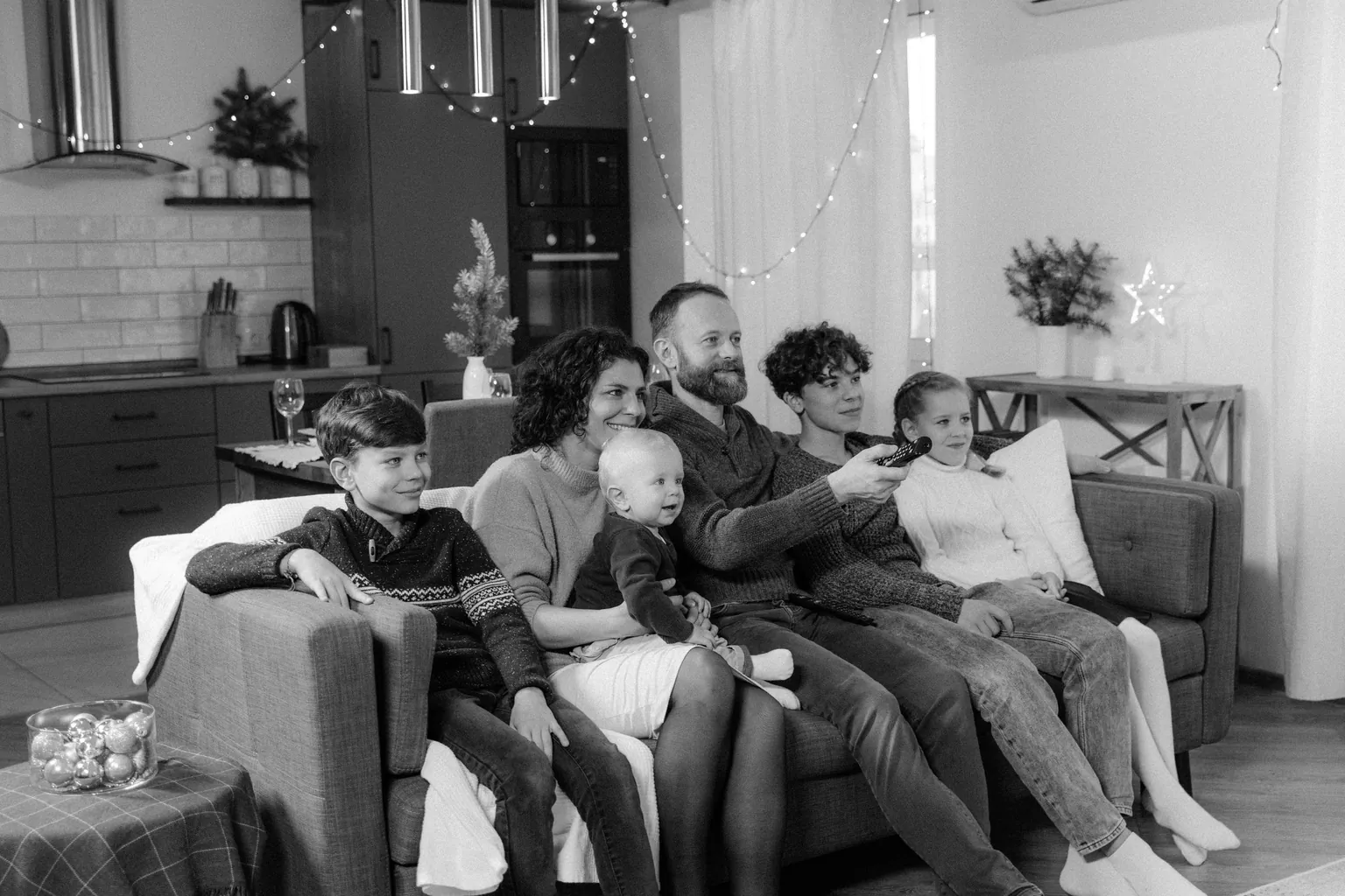 Famille de six personnes assise sur un canapé devant la télévision, photo en noir et blanc