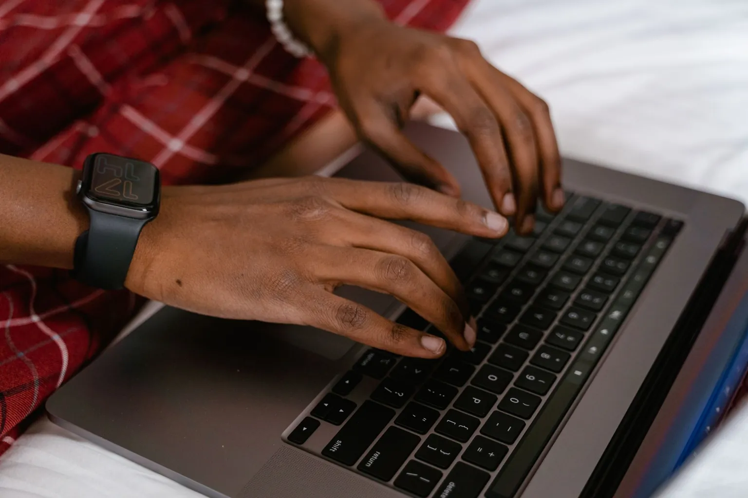 Mains tapant sur le clavier d'un ordinateur portable posé sur un lit